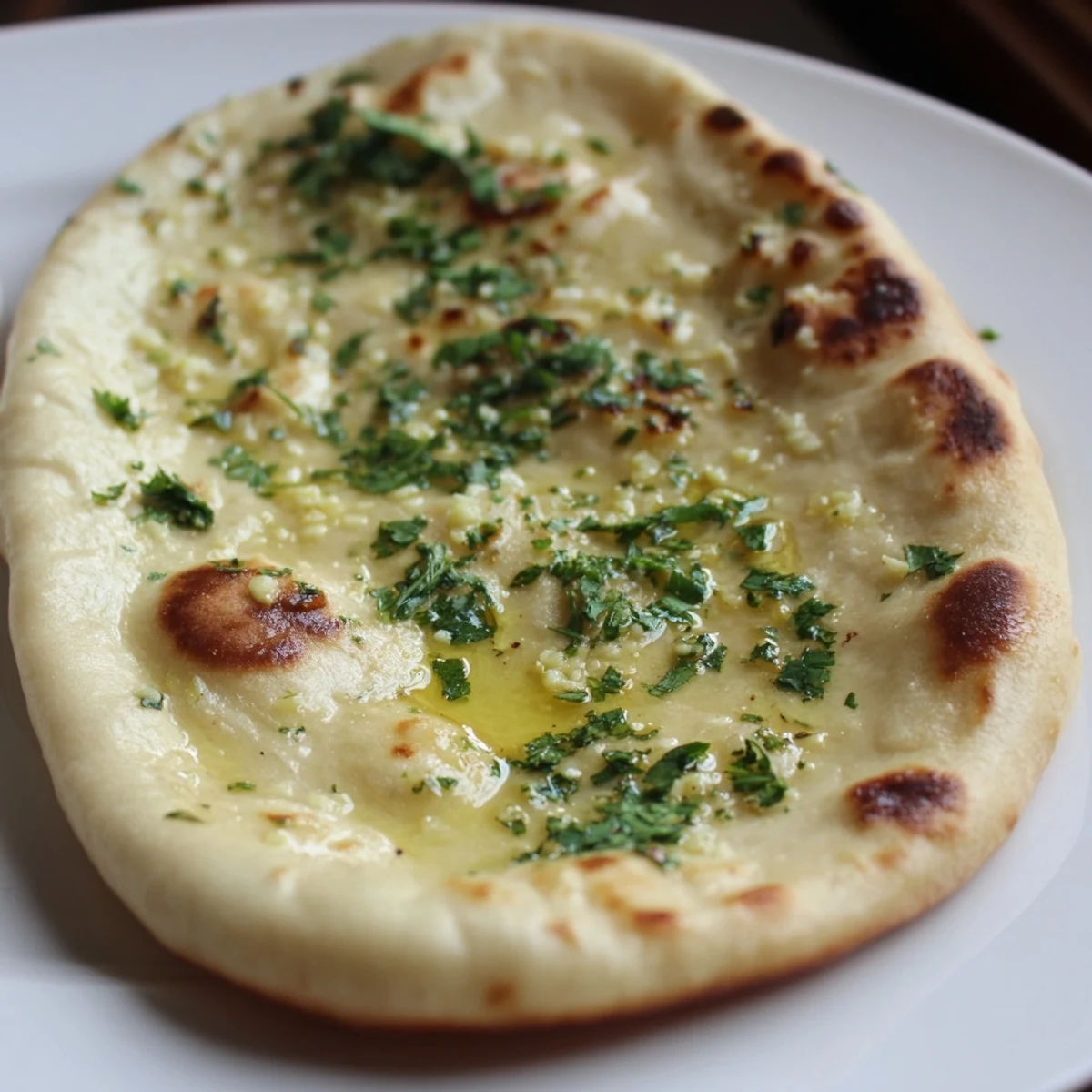 Warm, buttery garlic naan bread, with visible flecks of cilantro, fresh from the skillet.
