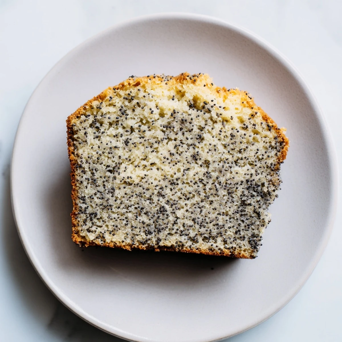 A close-up of a golden poppy seed cake slice, perfect with fresh berries and whipped cream.