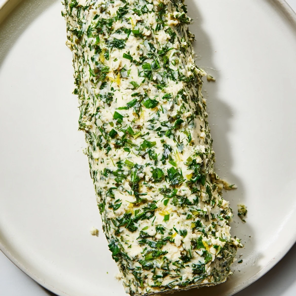 Creamy herb butter, speckled with fresh green herbs, ready to be sliced and served alongside warm bread.