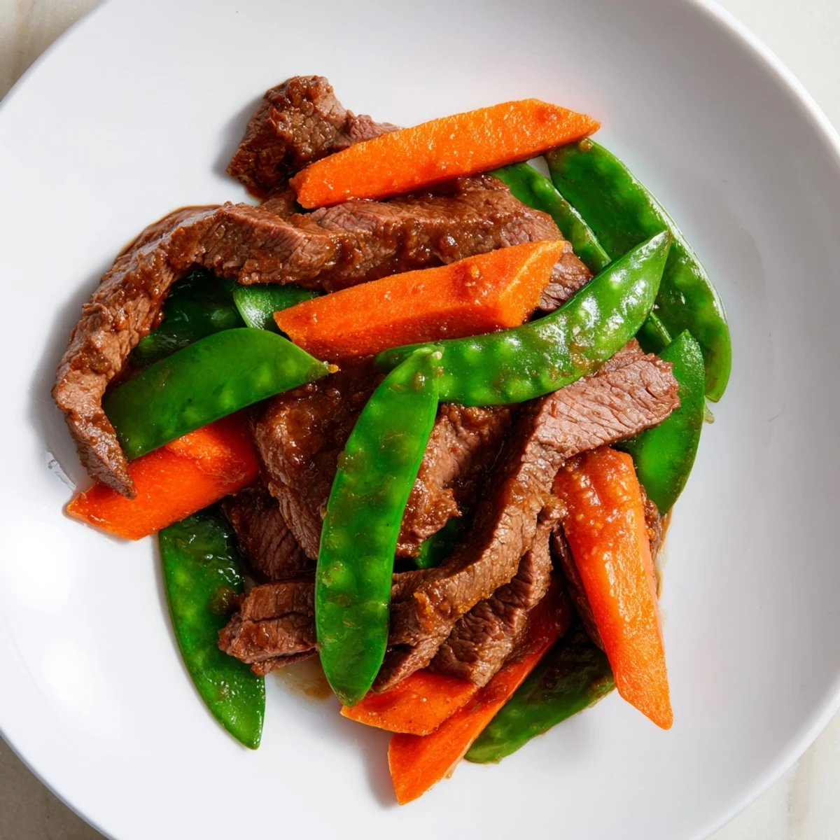 Freshly cooked Beef Stir Fry with Snow Peas and Carrots is served hot over steamed white rice in a ceramic bowl.