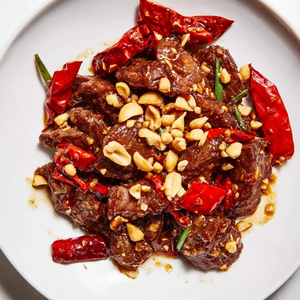 Freshly chopped peanuts and sliced green onions garnish a sizzling wok of Spicy Szechuan Beef, highlighting the dish's crunchy texture.