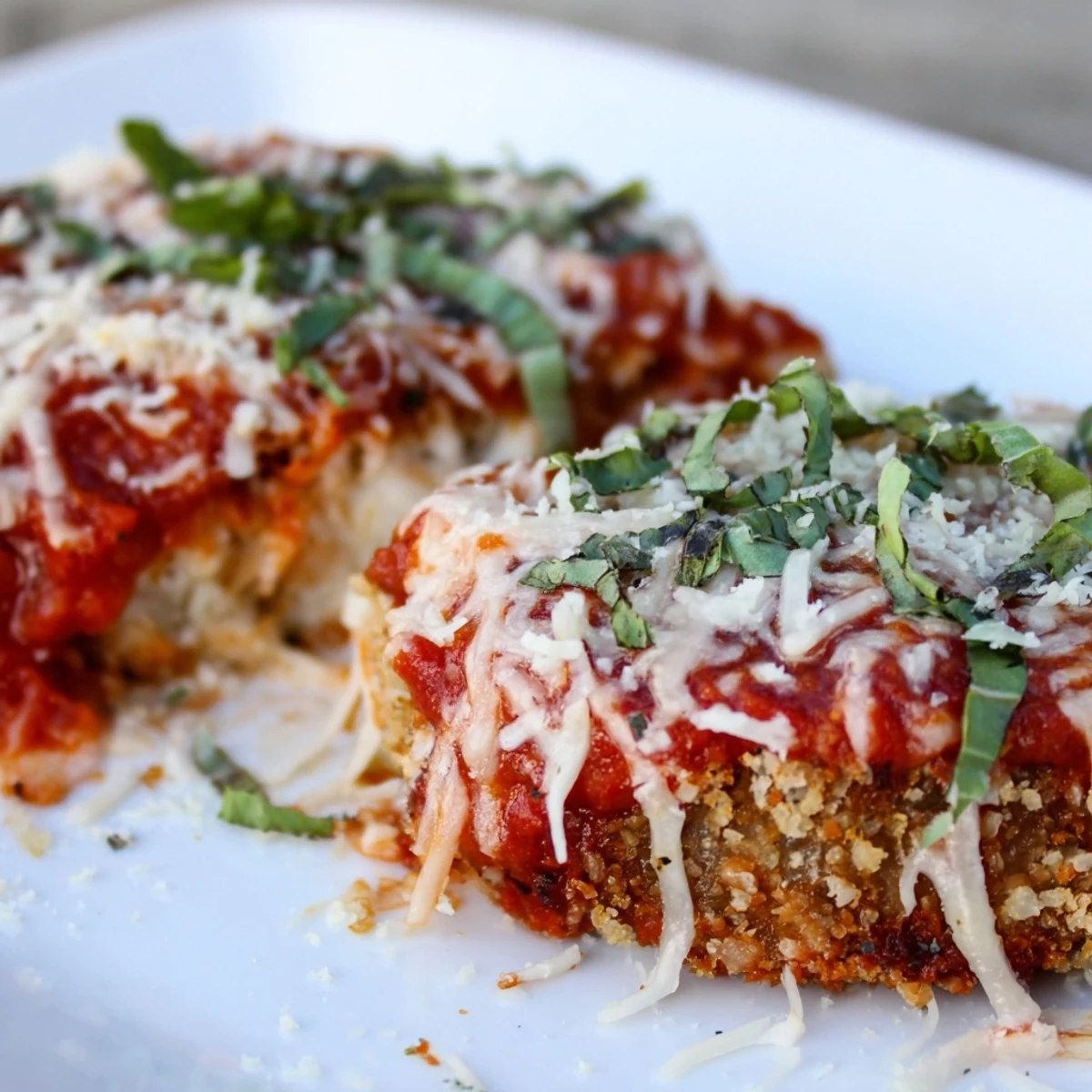A close-up of golden Baked Eggplant Parmesan with bubbly cheese, tomato sauce, and torn basil garnish on top.