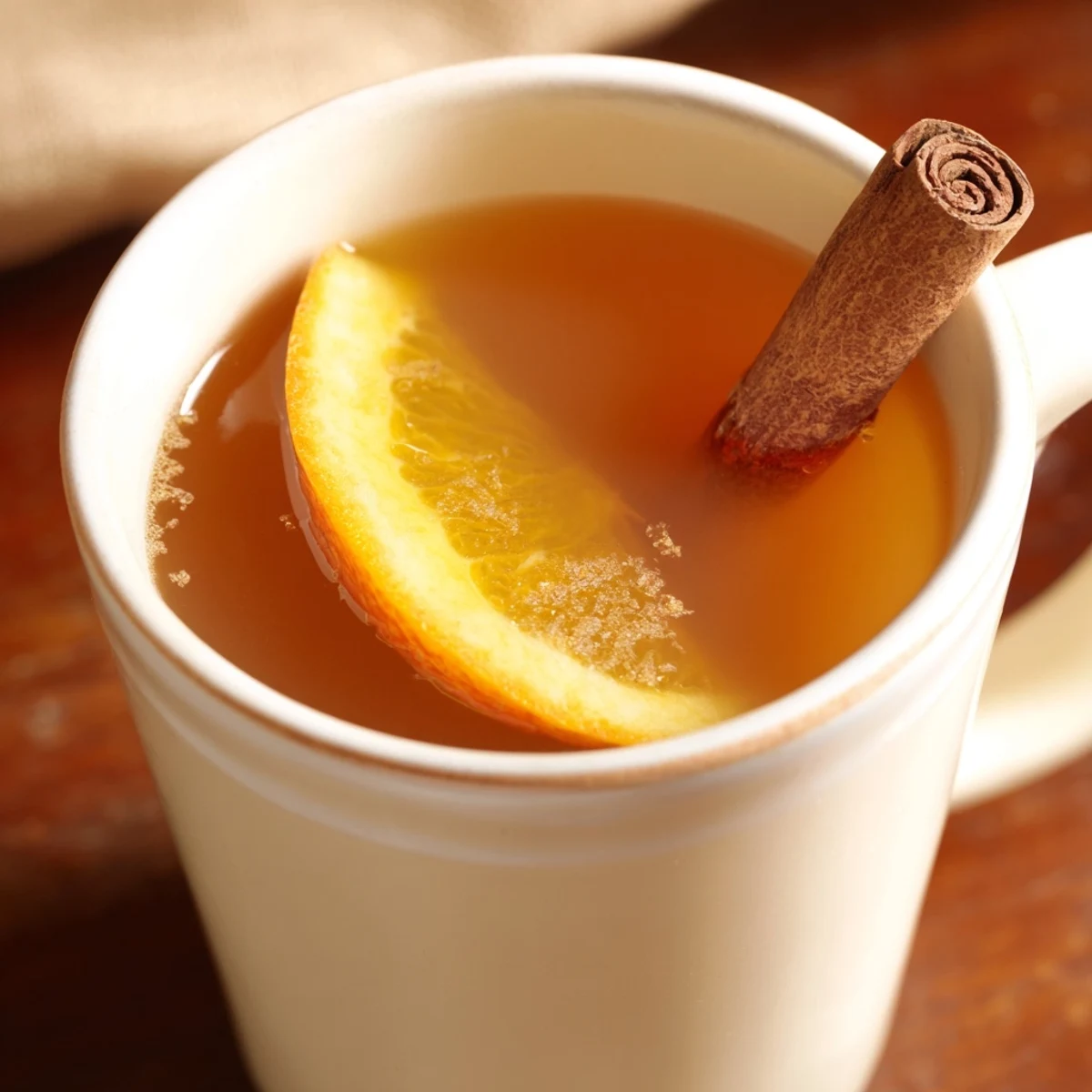 Steaming mugs of spiced hot apple juice with cinnamon glow warmly beside simmering spices and orange slices.