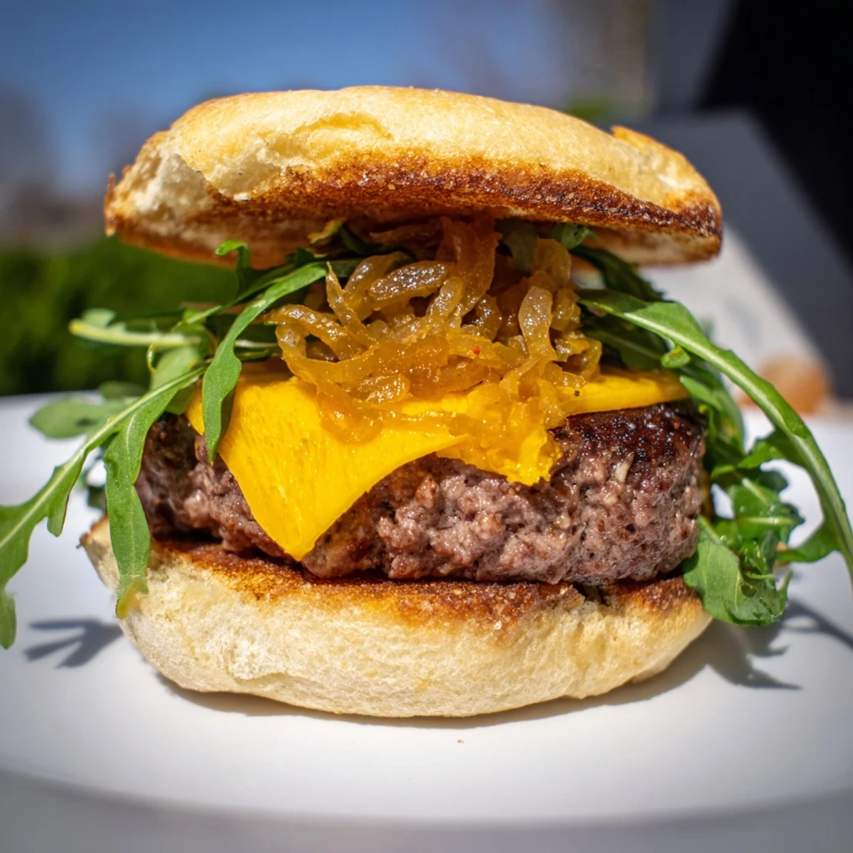 Golden brown Beef Sliders with Caramelized Onions and Cheddar on a platter, topped with arugula.