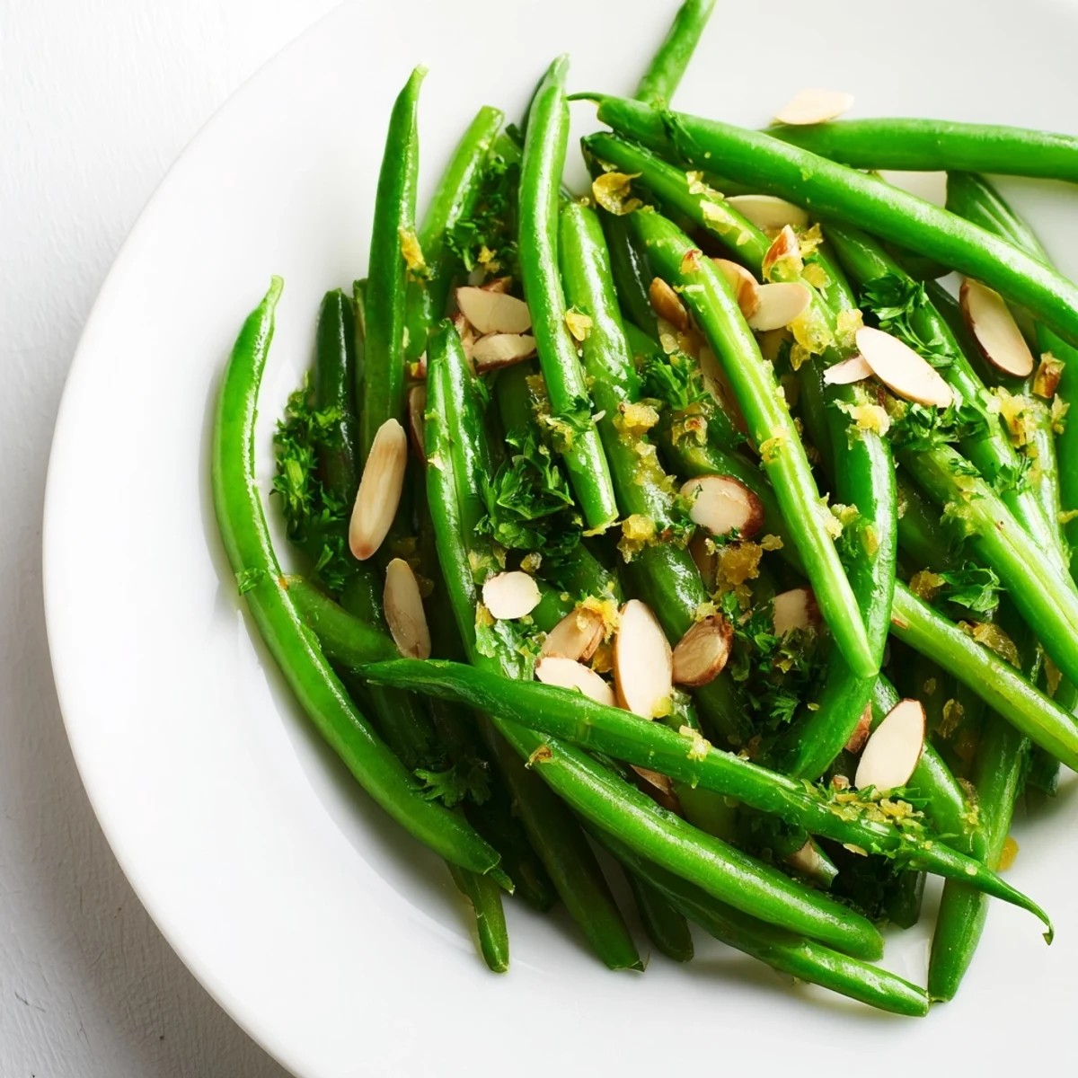Crisp-tender Lemon Green Beans with minced garlic garnished with parsley and toasted almonds on a white platter.