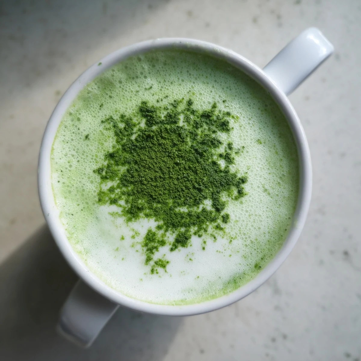 Close-up of a smooth Shamrock Green Matcha Latte with honey, garnished with edible gold flakes and a wooden stirring spoon nearby.