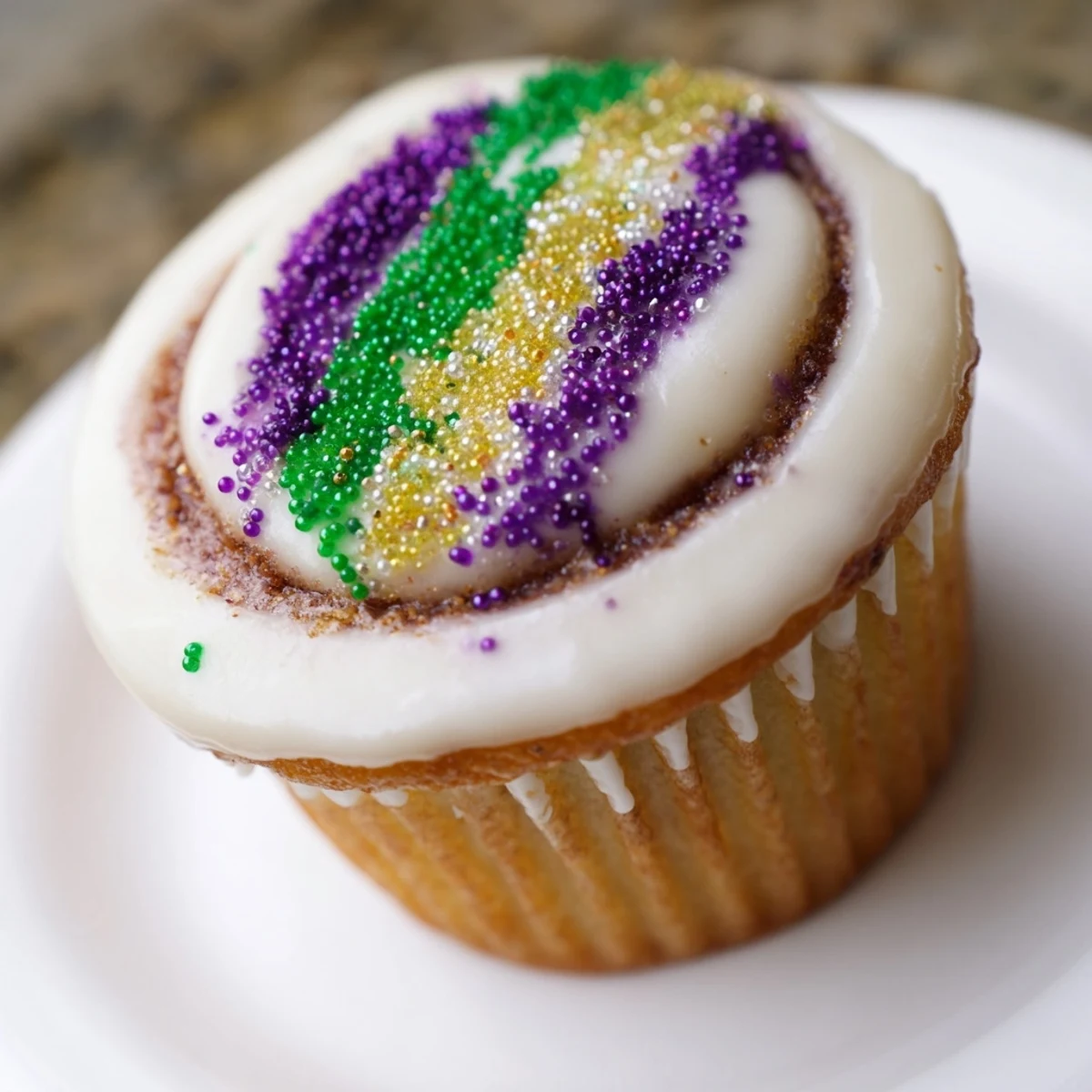 Cinnamon-swirled vanilla cupcakes topped with sweet glaze and colorful sugar for a festive Mardi Gras treat.