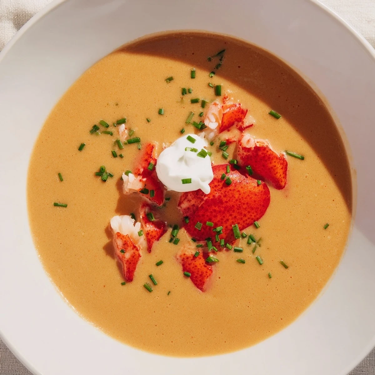 Silky Romantic Lobster Bisque in a white bowl, topped with fresh chives and lobster meat.