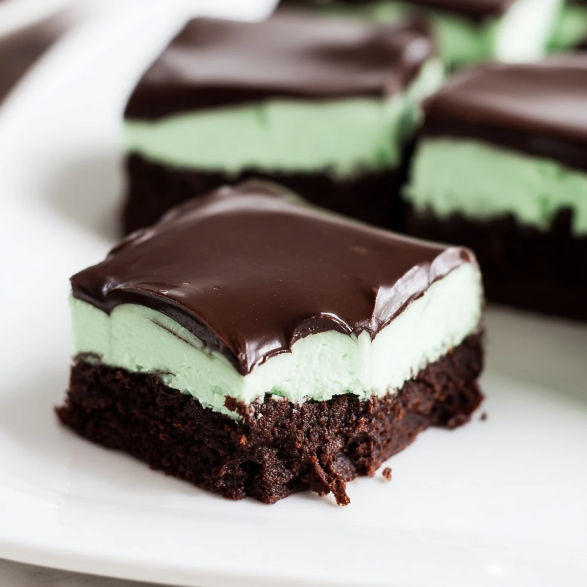 Fudgy Shamrock Mint Brownies with Chocolate Ganache are arranged on a white plate, with a small glass of cold milk in the background.