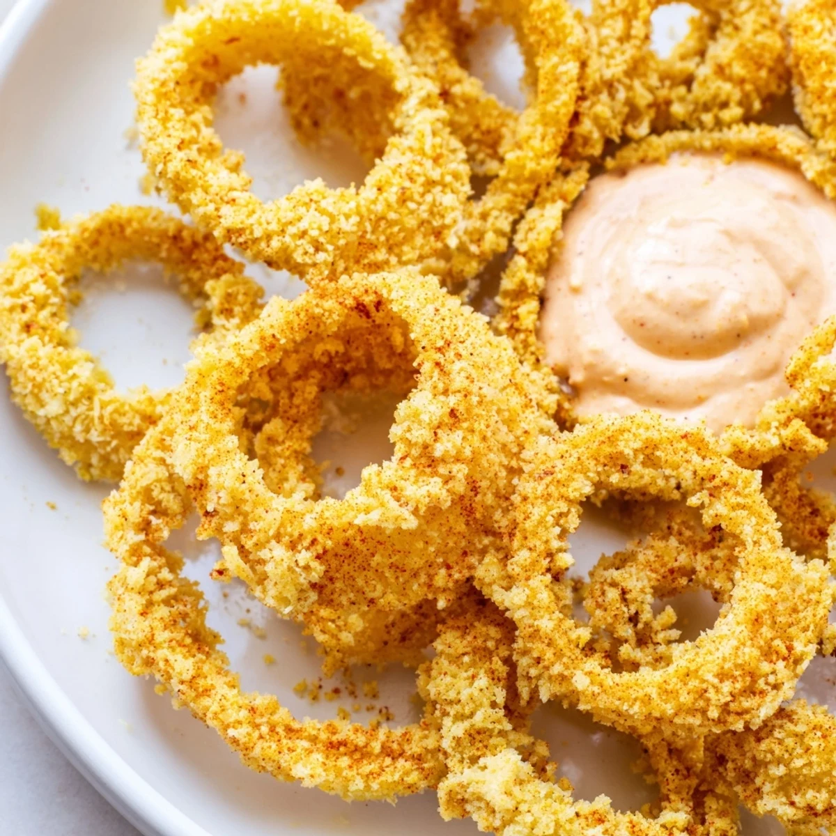 Freshly cooked air fryer onion rings with golden breading, paired with creamy chipotle mayonnaise for dipping.  