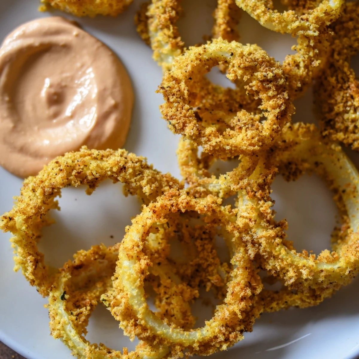 Crispy air fryer onion rings stacked high, accompanied by a bowl of spicy chipotle mayo for snacking.