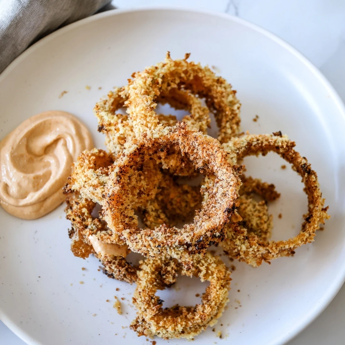 Stacks of golden Crispy Air Fryer Onion Rings with Chipotle Mayo on a plate next to a small ramekin of smoky dip.