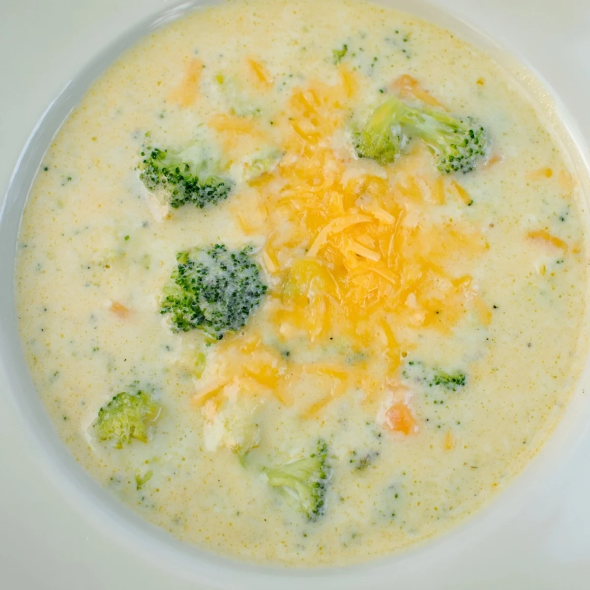 Steam rises from a serving of Creamy Broccoli Cheddar Soup, paired with a slice of crusty bread for dipping.