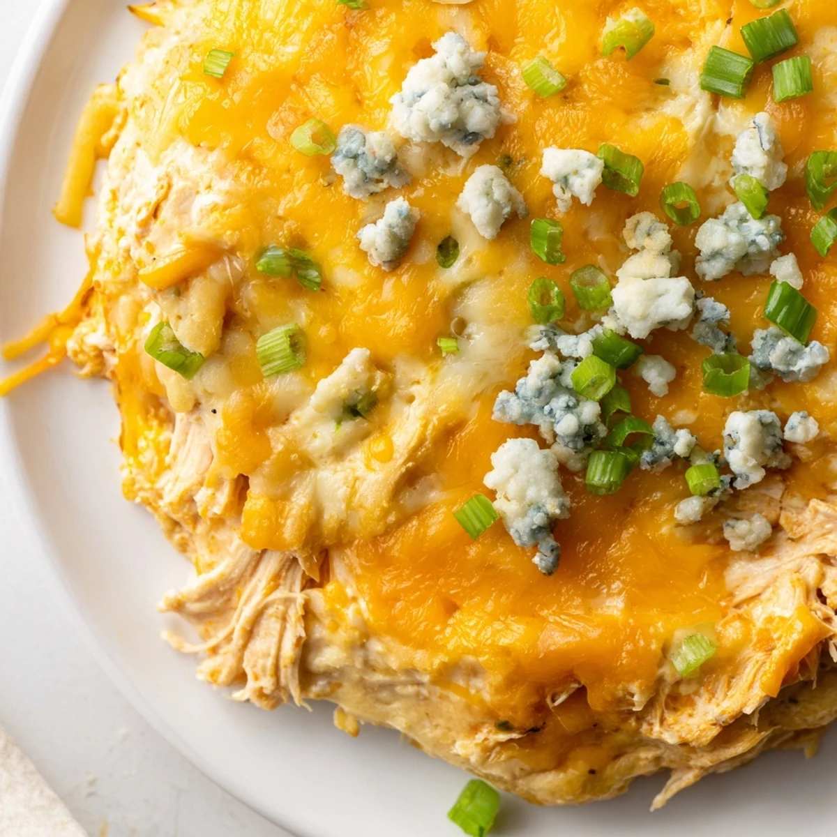 Golden, bubbly Keto Buffalo Chicken Dip served warm in a baking dish, garnished with fresh green onions and crumbled blue cheese.