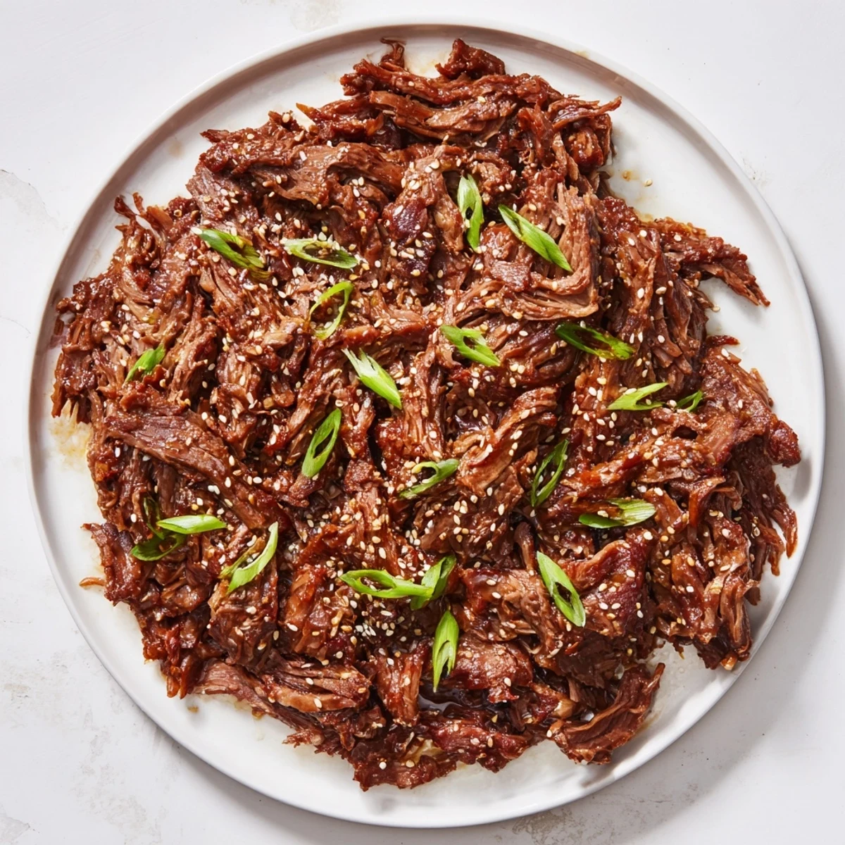 Slow Cooker Korean Beef served in a shallow bowl over fluffy white rice, garnished with sesame seeds and a side of kimchi for extra crunch.