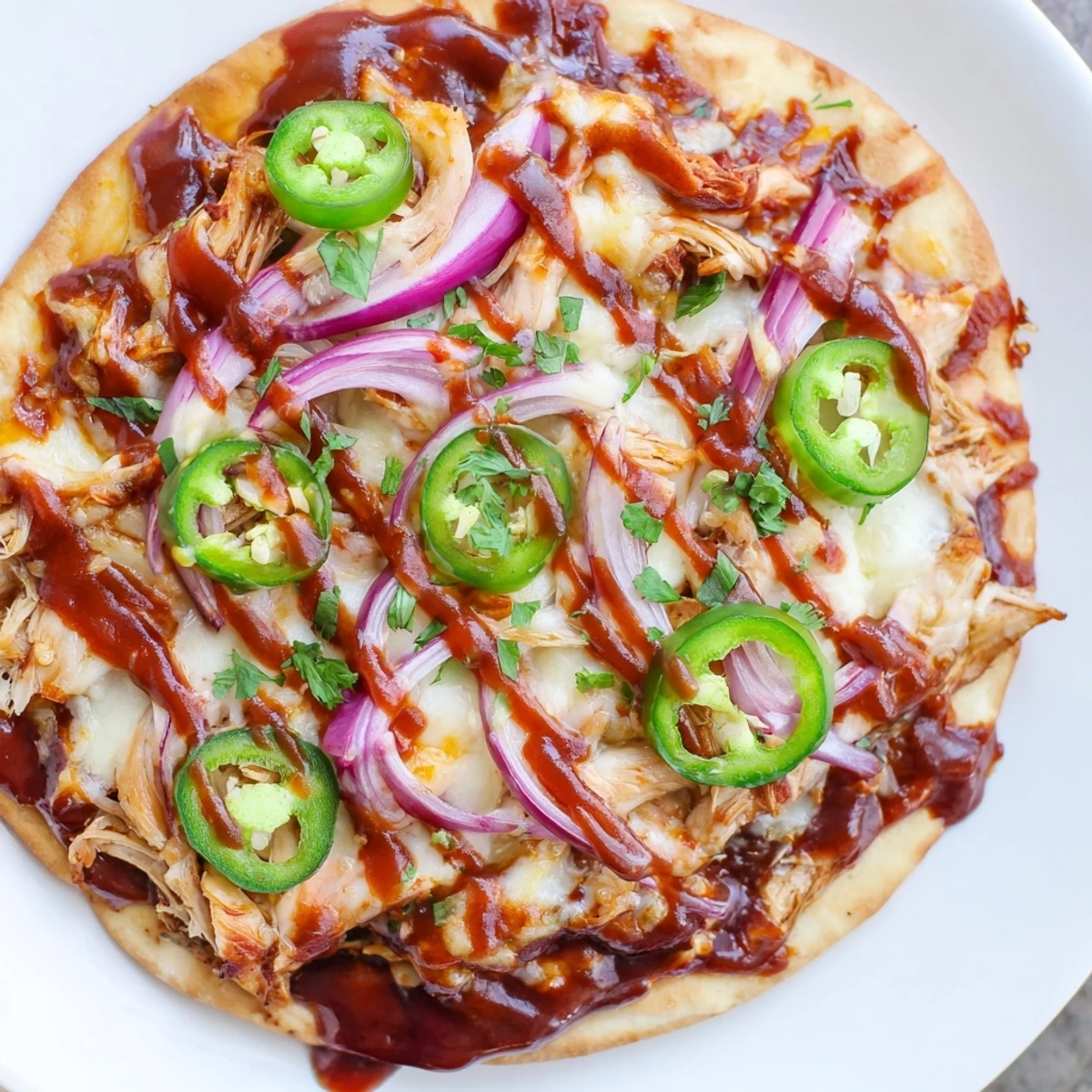 Golden BBQ Chicken Flatbread topped with melted mozzarella and cheddar cheese, red onion slices, and fresh jalapeños on a baking sheet.