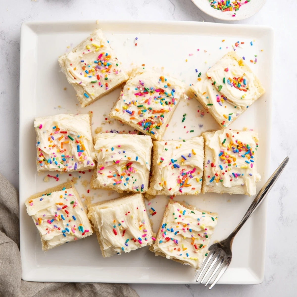 Golden-baked Sugar Cookie Bars with fluffy vanilla frosting and colorful sprinkles on a white plate, ready to serve at a party.