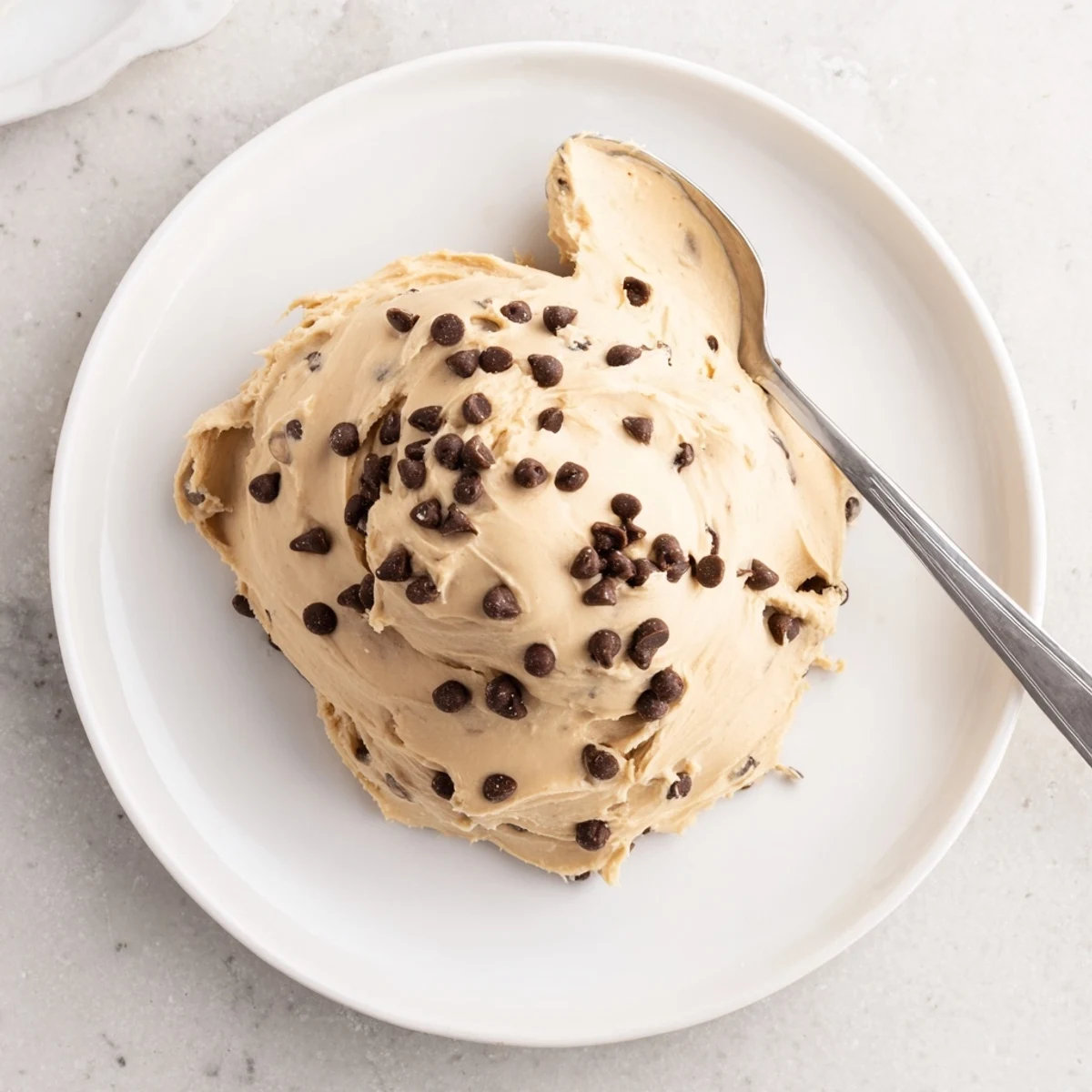 A close-up of rich, creamy Cookie Dough Frosting with mini chocolate chips, ready to spread on cupcakes.