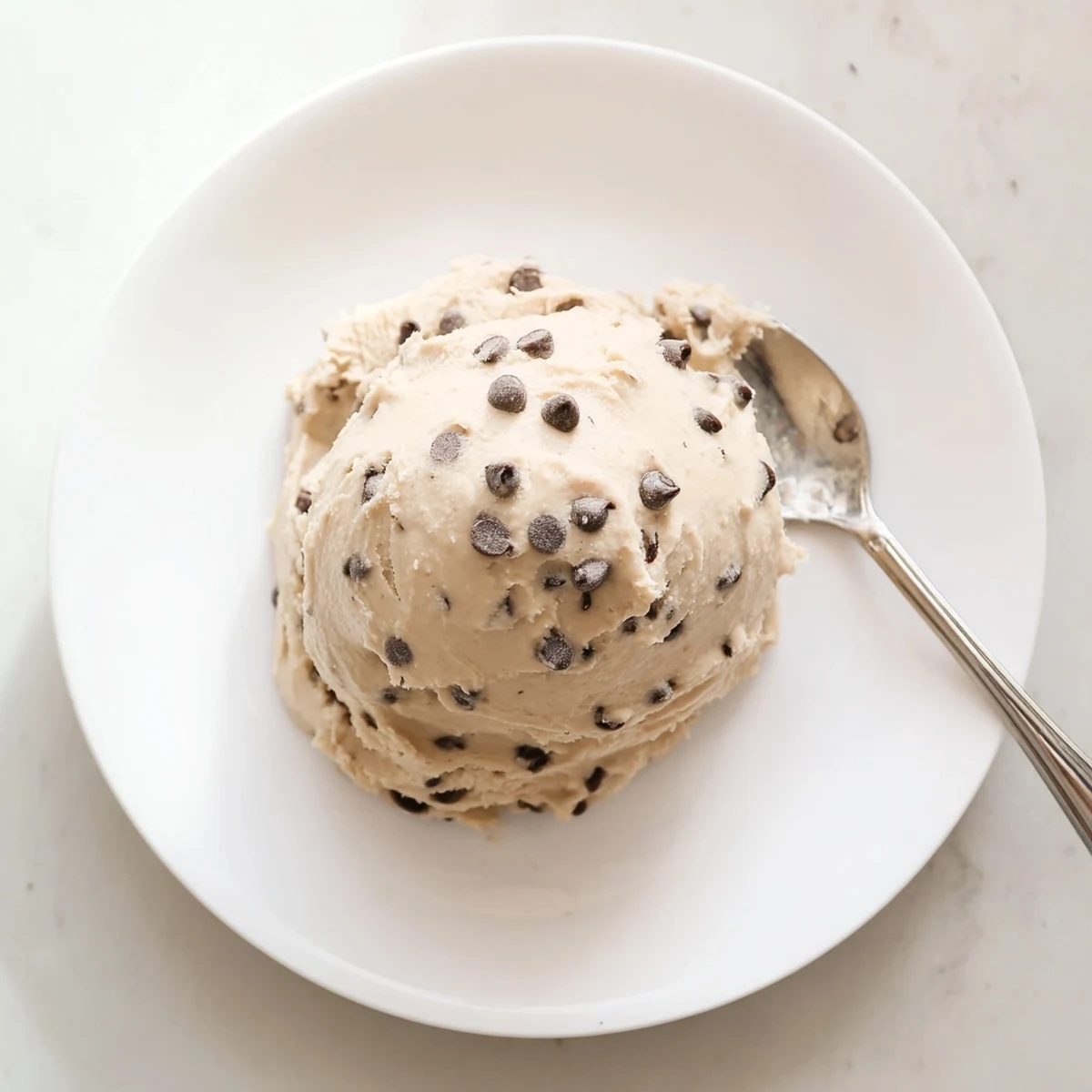 Glossy Cookie Dough Frosting swirled on a spatula, showing off its soft, doughy texture and vanilla scent.