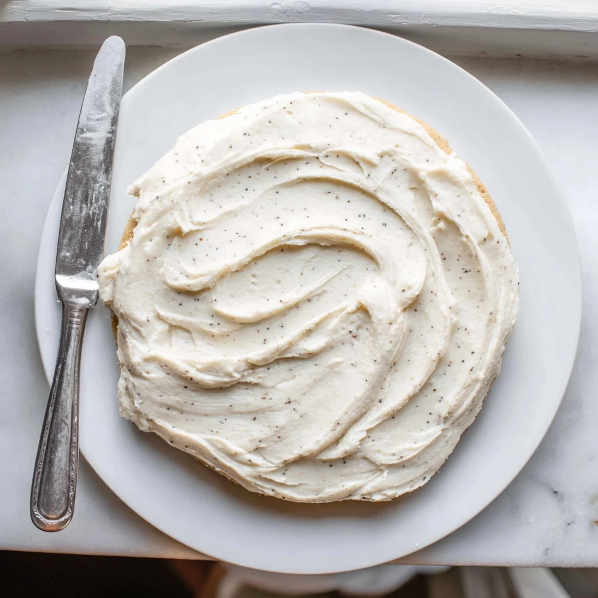 Creamy vanilla Easy Sugar Cookie Frosting spreading smoothly over fully cooled sugar cookies.
