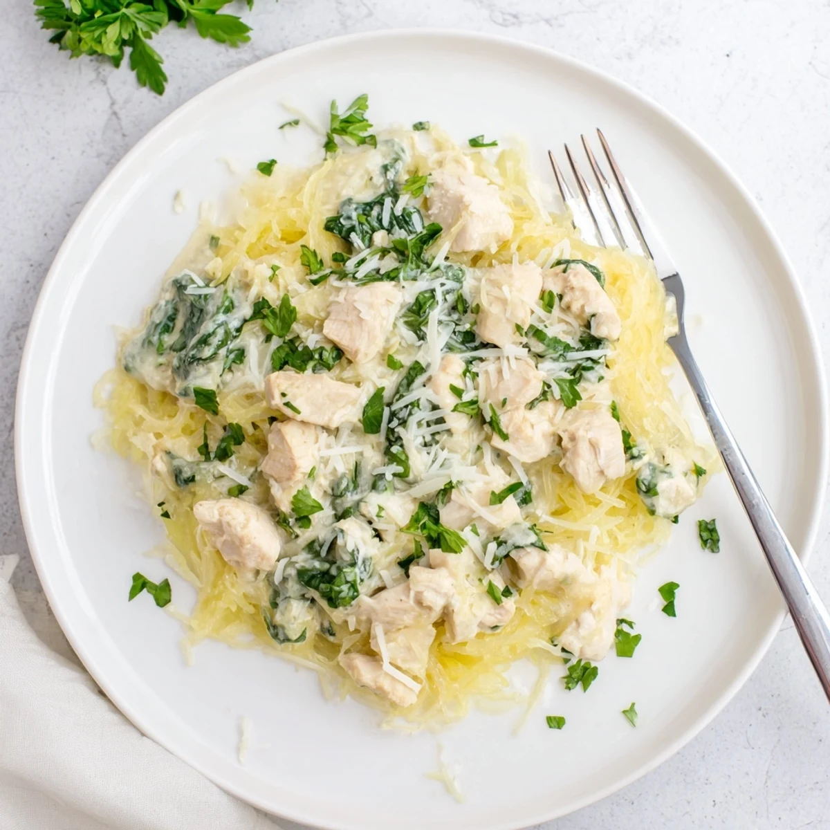 Golden roasted spaghetti squash strands are tossed with tender diced chicken and fresh spinach in a creamy garlicky Alfredo sauce, garnished with parsley.