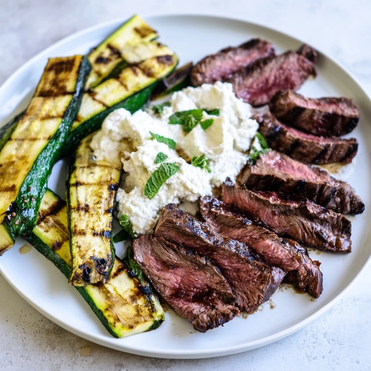 Juicy balsamic flank steak and smoky grilled zucchini topped with creamy whipped feta on a serving platter.