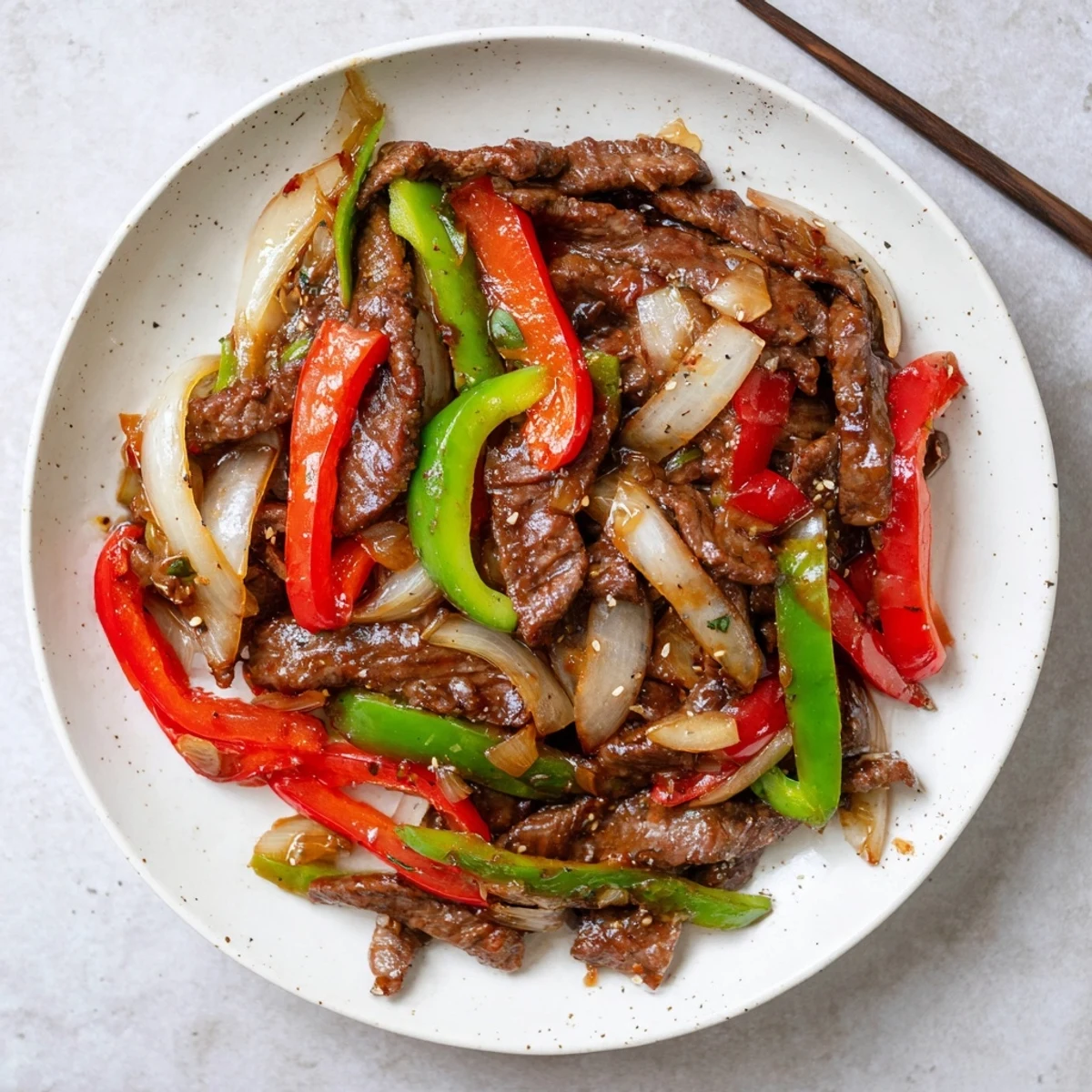 Freshly stir-fried Sizzling Chinese Pepper Steak With Onions on a plate, onions and bell peppers glistening in sauce.
