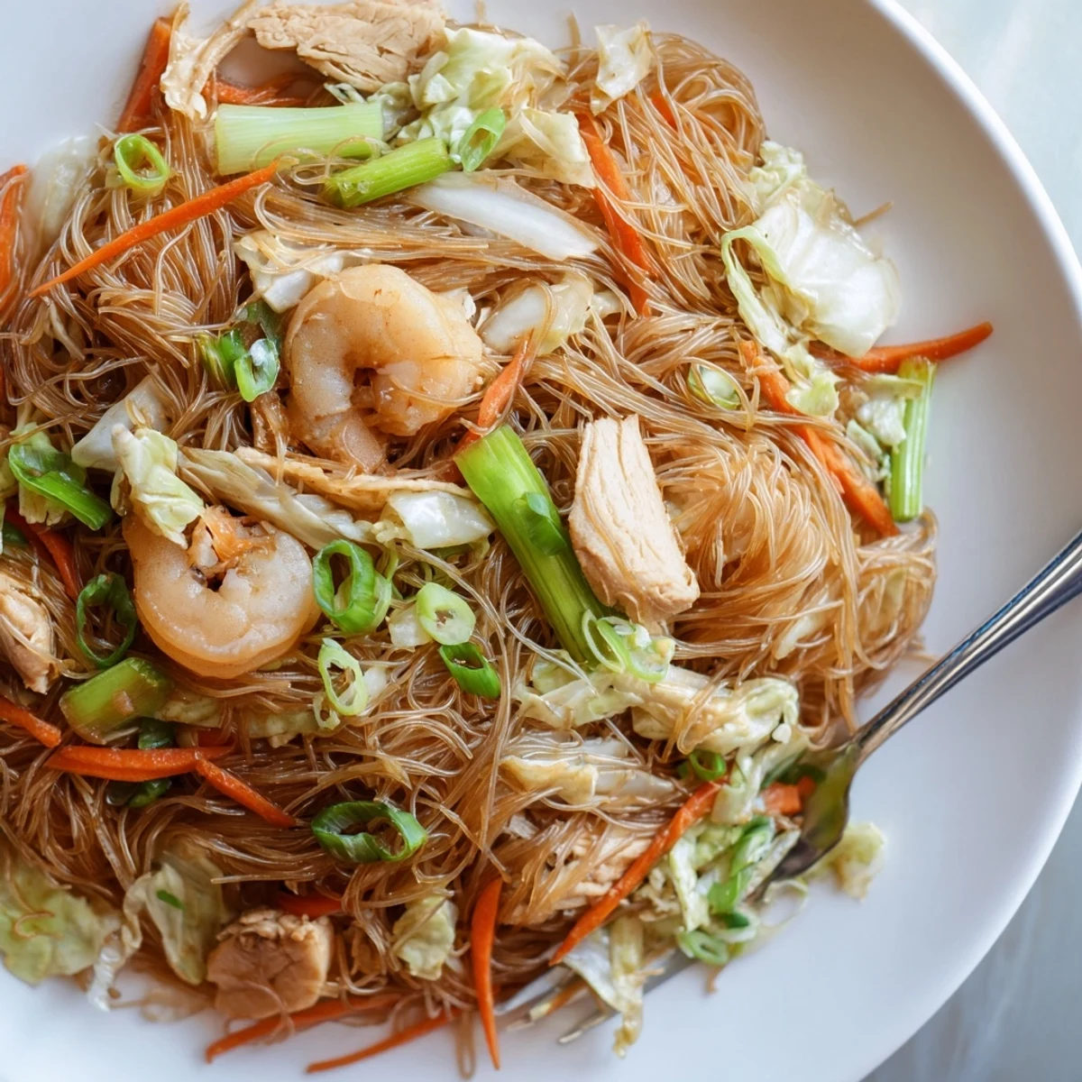 Golden plate of savory Traditional Pancit Bihon garnished with fresh scallions and lemon wedges