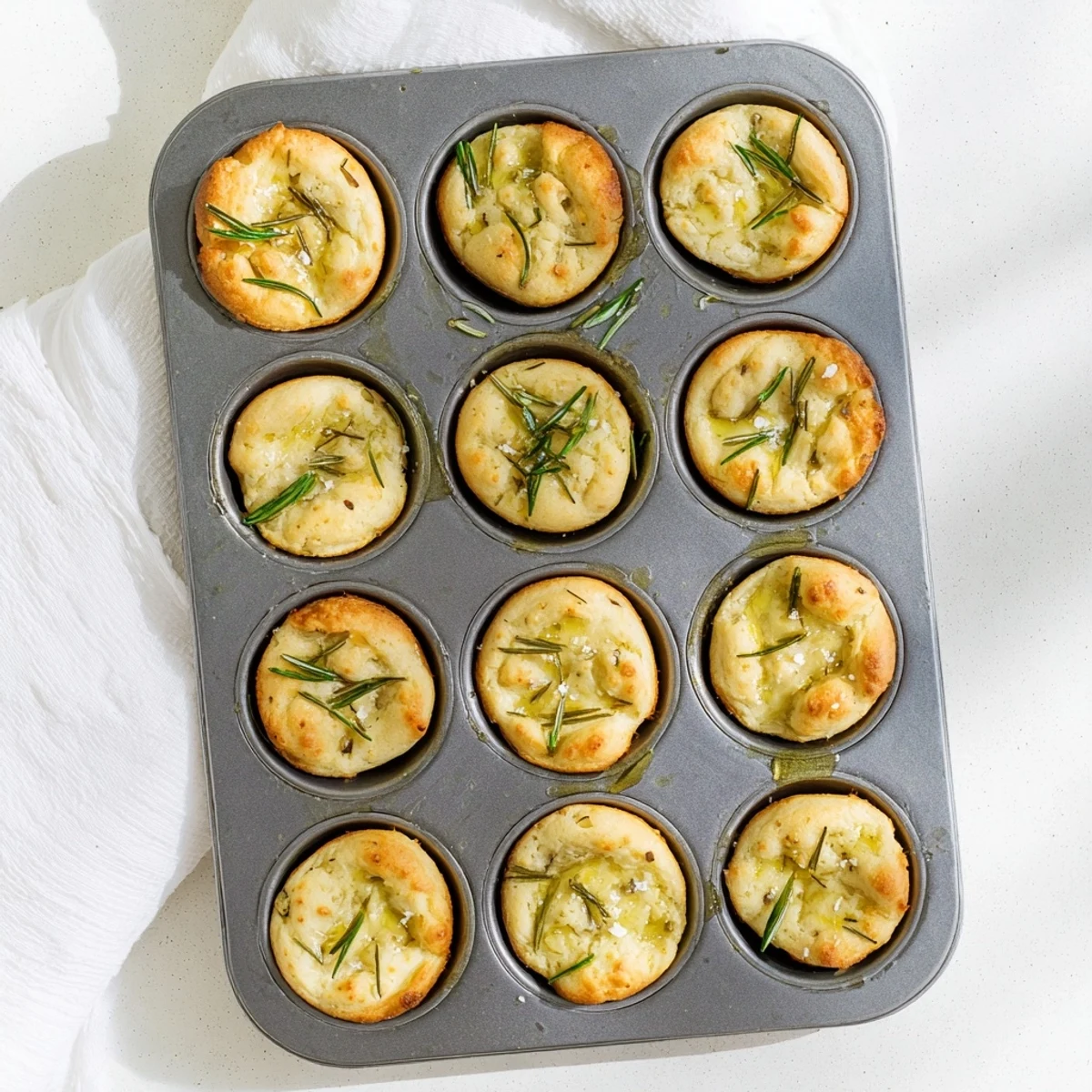Golden brown garlic rosemary focaccia muffins topped with fresh herbs and sea salt