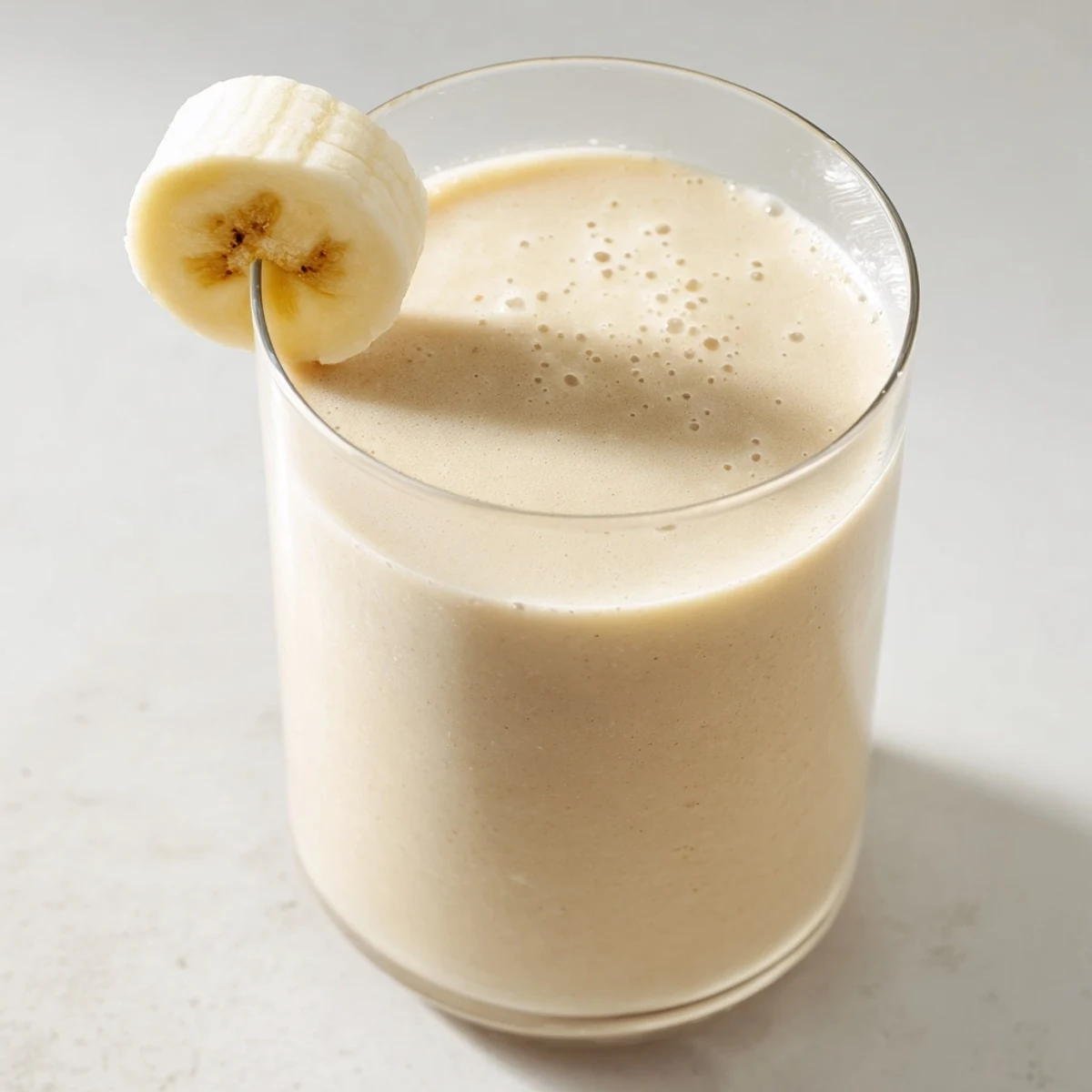 Creamy Greek yogurt banana smoothie poured into tall glasses with sliced banana garnish on top
