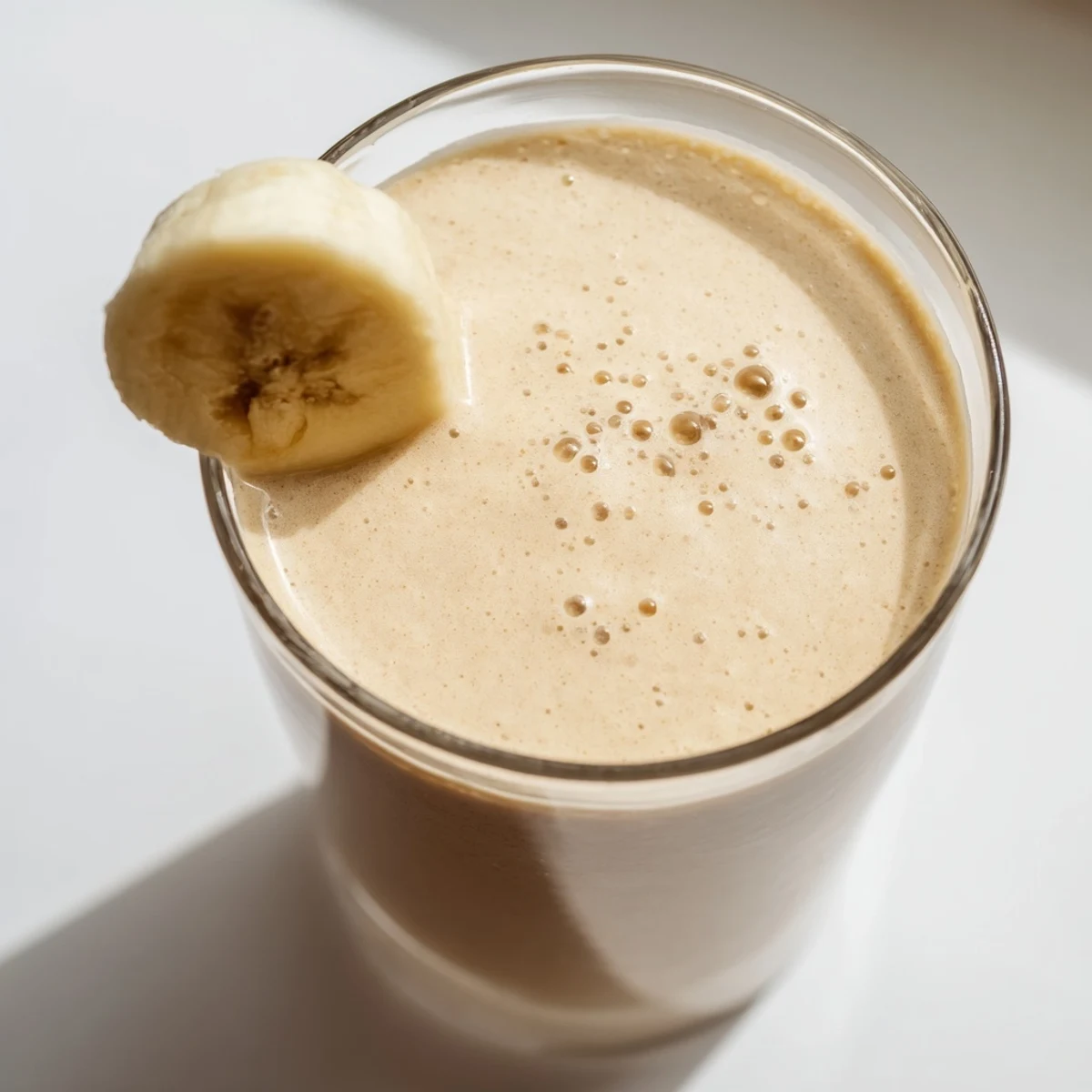 Golden Greek yogurt banana smoothie in a clear glass showcasing its smooth velvety texture