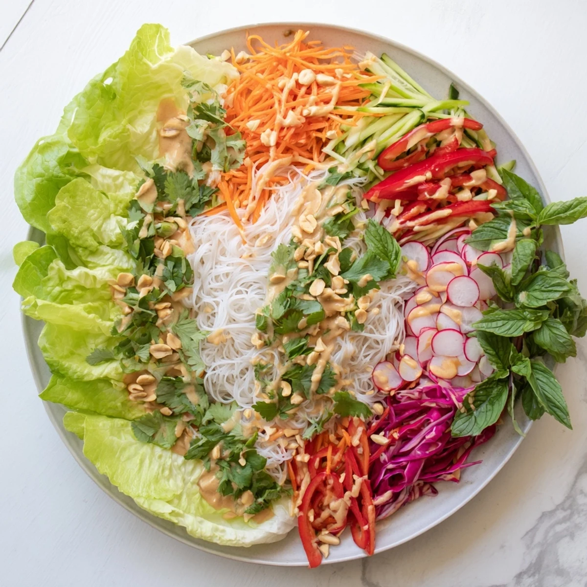 Fresh spring roll salad with peanut drizzle topped with crushed peanuts, cilantro, and mint over crisp butter lettuce leaves