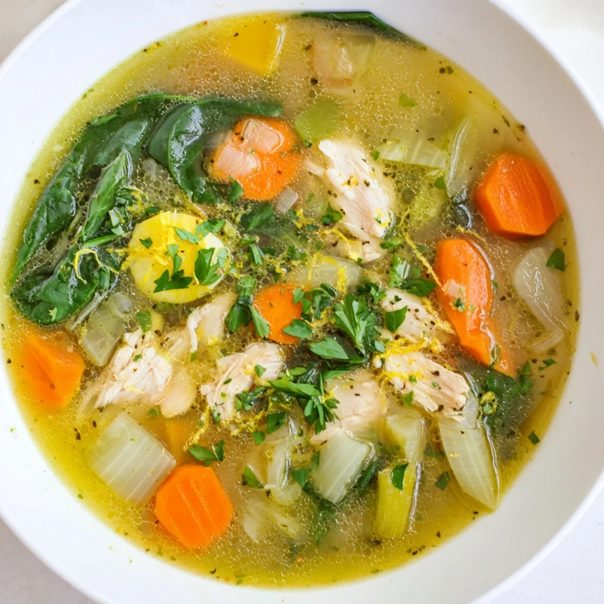 Steaming pot of zesty lemon herb chicken soup featuring carrots, celery, and vibrant green spinach