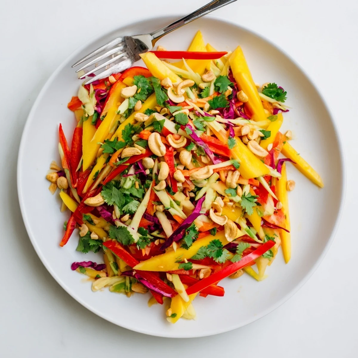 Fresh mango slaw topped with cilantro and crunchy cashews in a white bowl