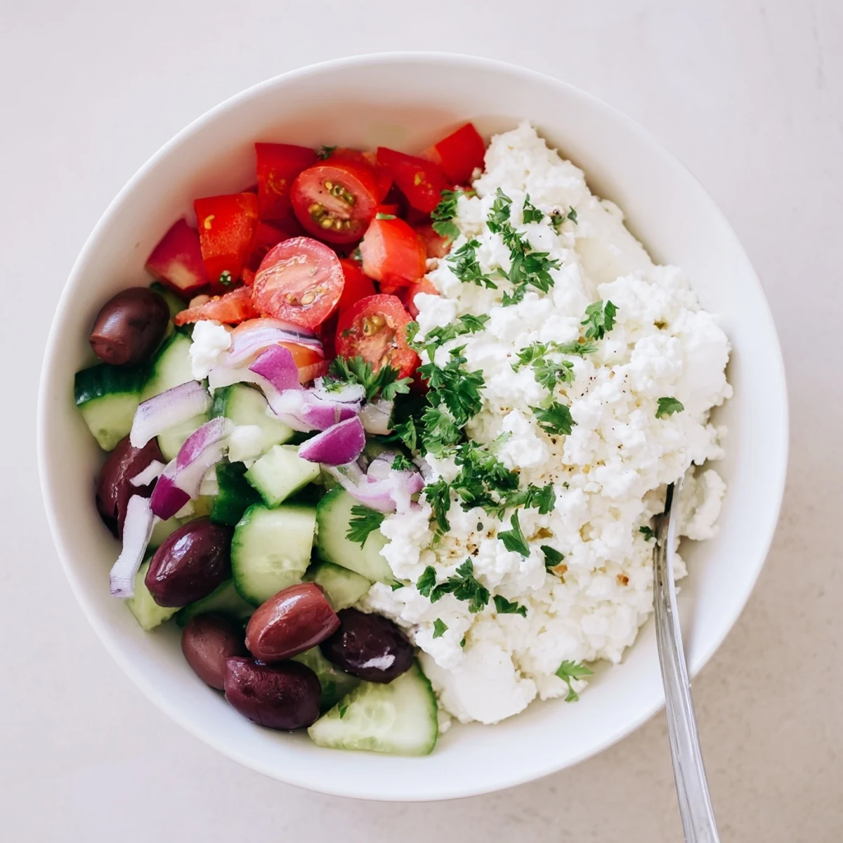 Colorful Greek salad cottage cheese bowl topped with fresh vegetables, olives, and crumbled feta