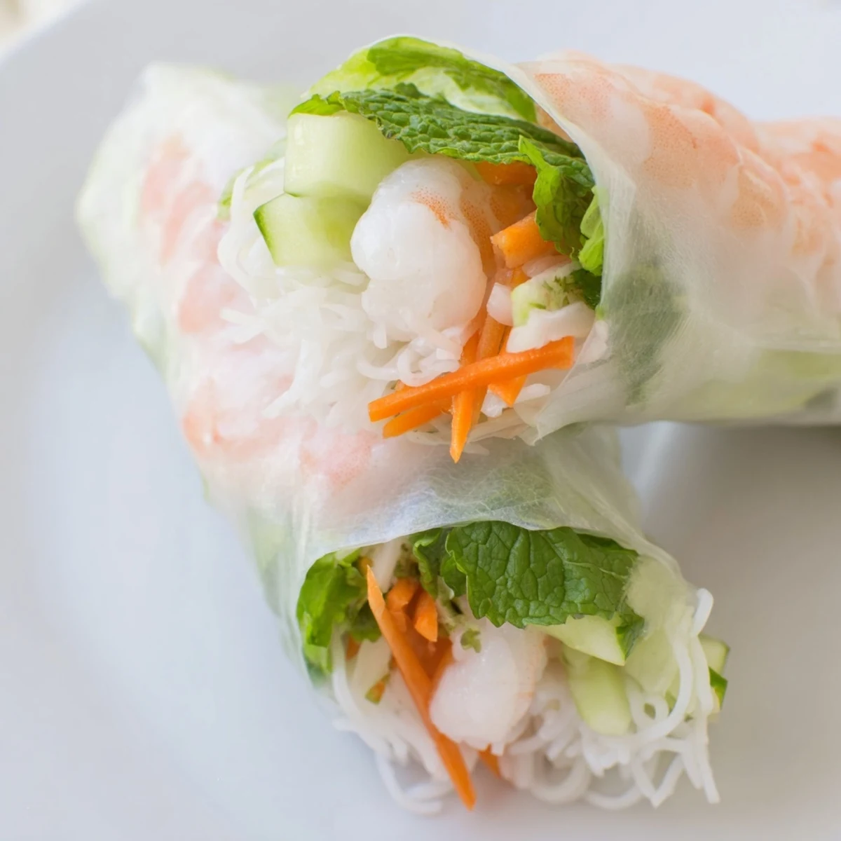 Homemade fresh spring rolls arranged on white plate with bowl of creamy peanut sauce and fresh mint garnish