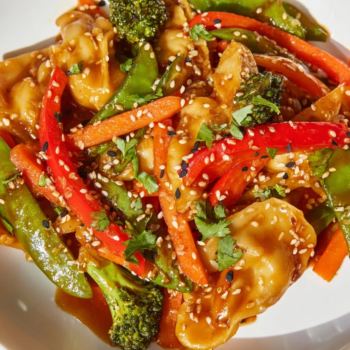 Plate of dumpling stir fry featuring snap peas and carrots coated in aromatic sauce