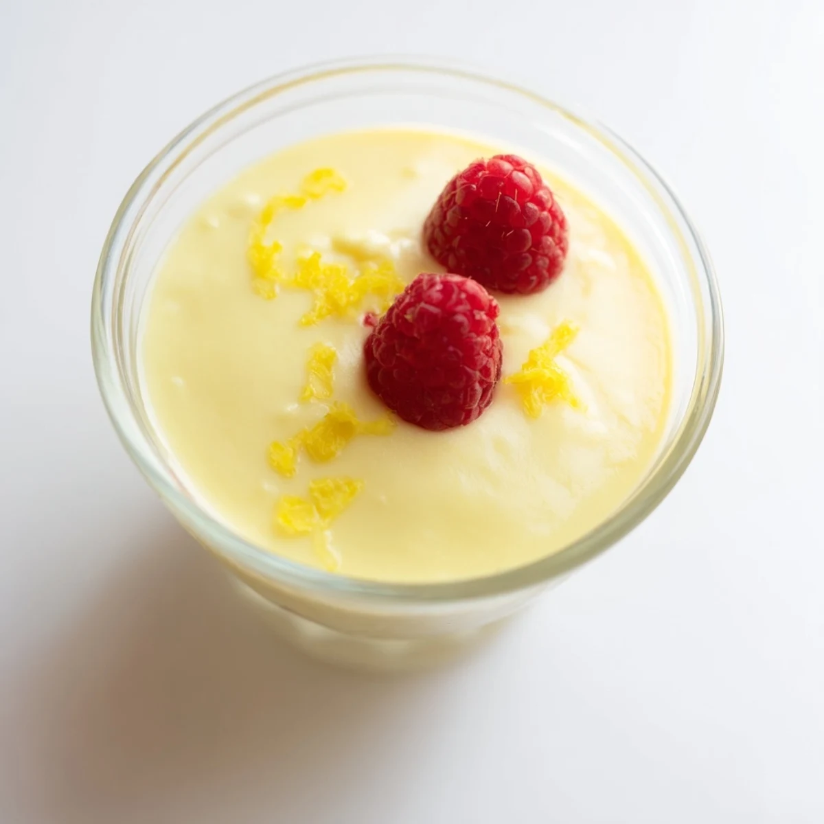 Silky smooth lemon posset set in clear glass with fresh berry garnish and zest
