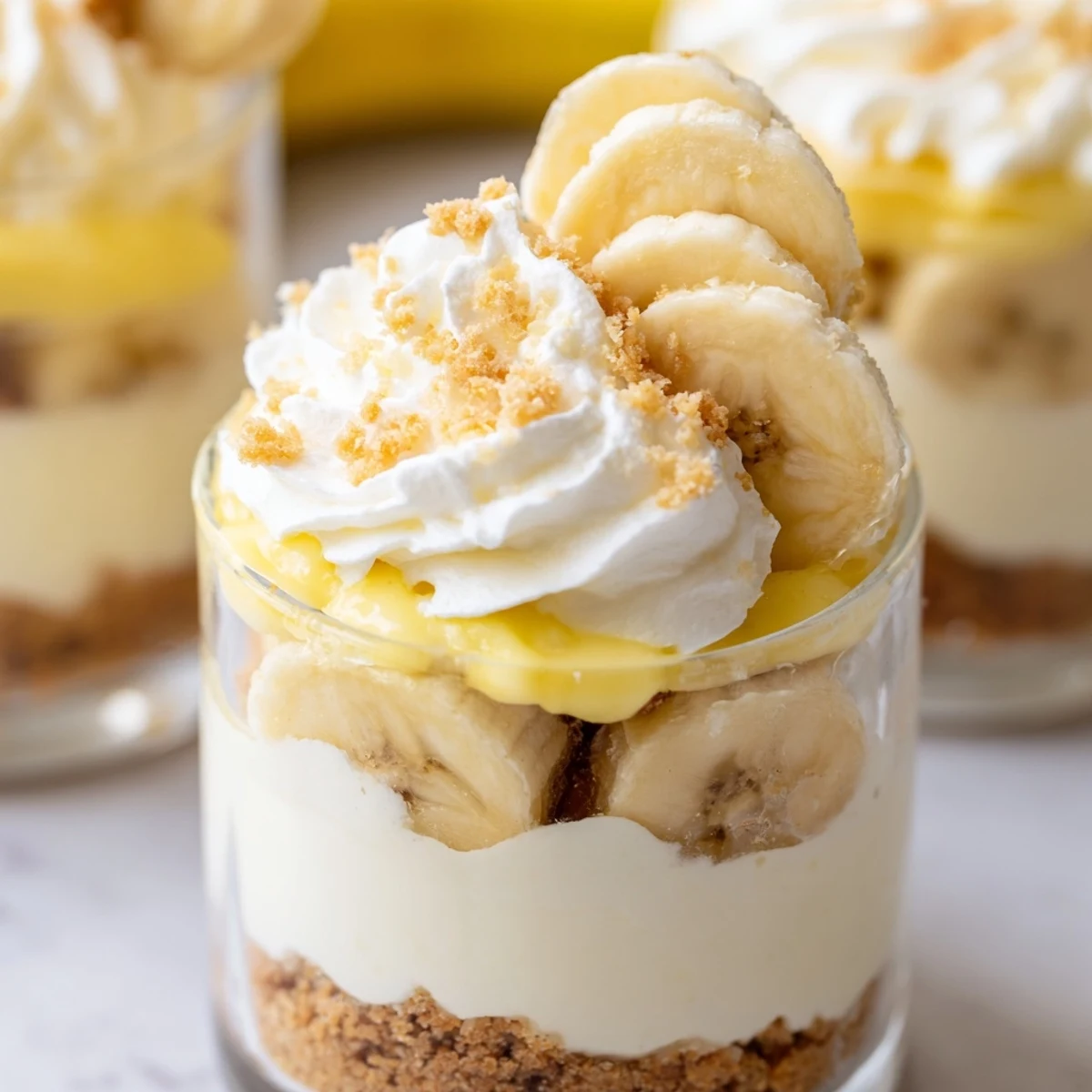 No bake banana pudding cheesecake cups topped with whipped cream and crunchy cookie crumbs