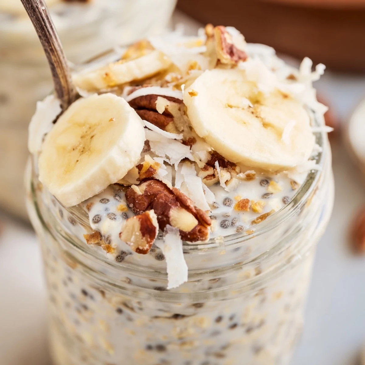 Thick coconut cream pie overnight oats layered with banana slices and crunchy almonds