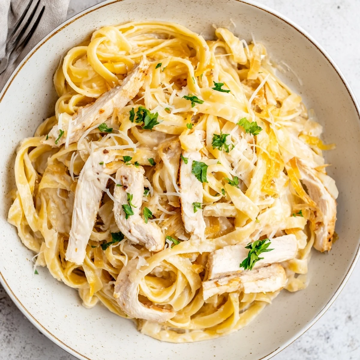 A fork twirls Creamy Garlic Chicken Pasta, fragrant sauce and Parmesan