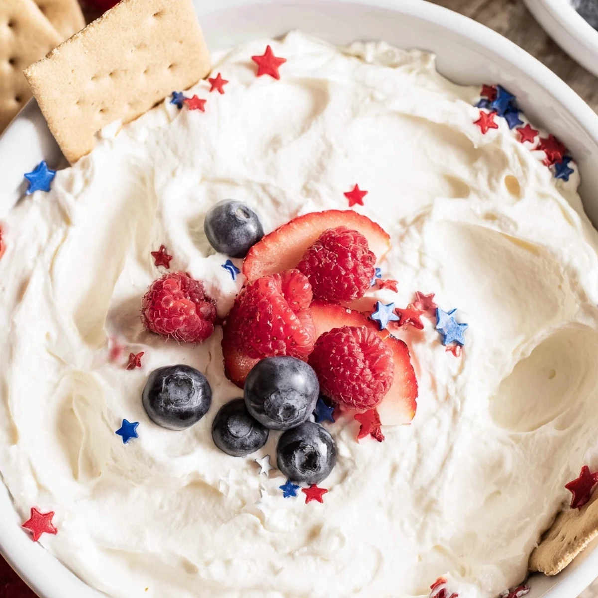 Light, fluffy Star Spangled Cheesecake Dip decorated with strawberries, blueberries, and pretzels