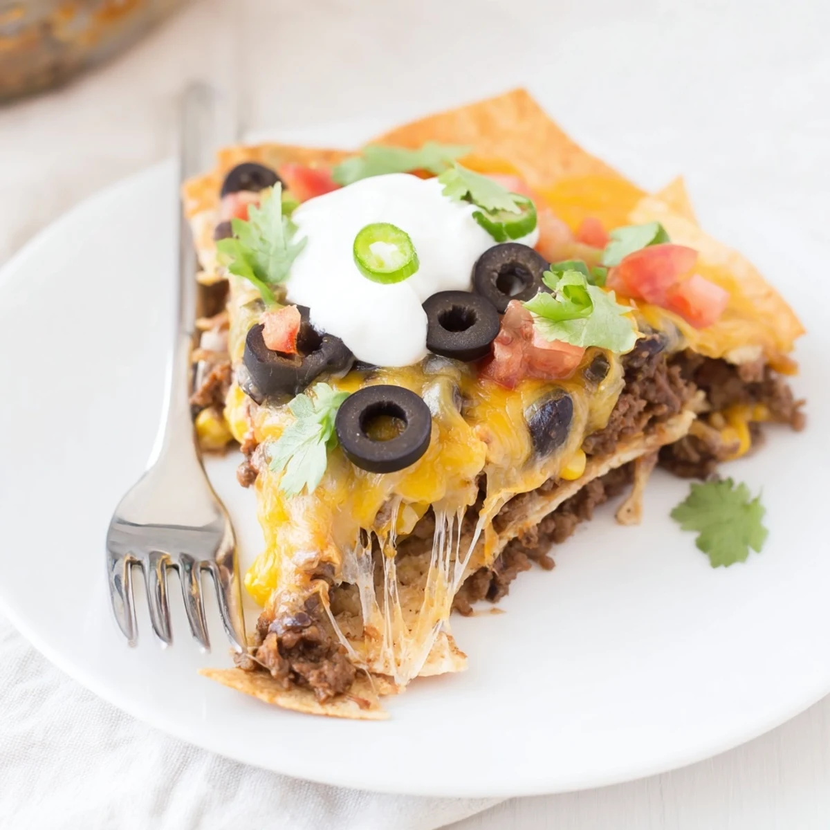 Cheesy Nacho Casserole oozing melted cheddar over crunchy tortilla chips, cilantro