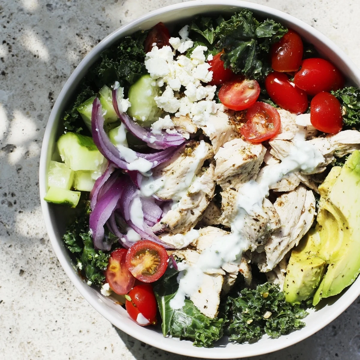 Colorful meal prep bowl featuring juicy marinated chicken over massaged kale with fresh vegetables