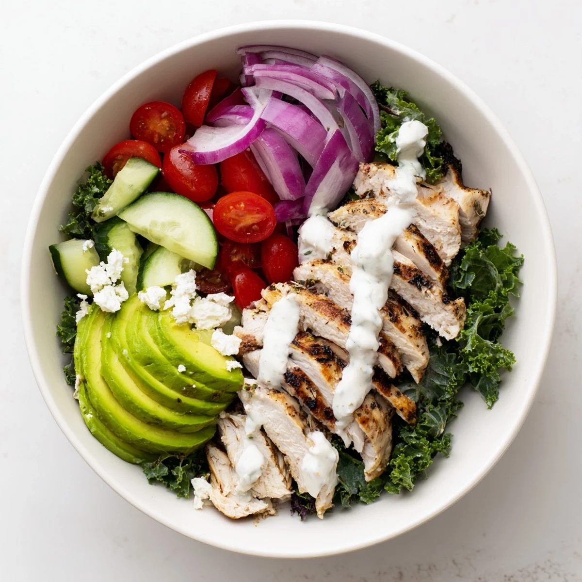 Healthy marinated kale and chicken bowls topped with avocado, tomatoes, and creamy homemade dressing