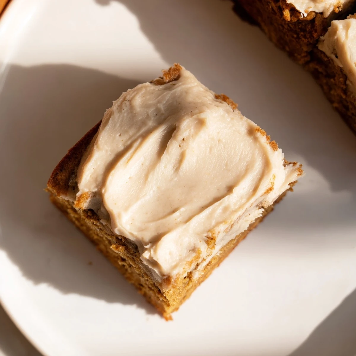 Thick banana bread brownies topped with swirls of nutty brown butter frosting on a white plate