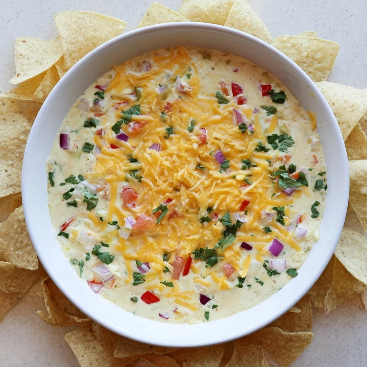 Golden green chile queso dip bubbling in a white bowl with tortilla chips