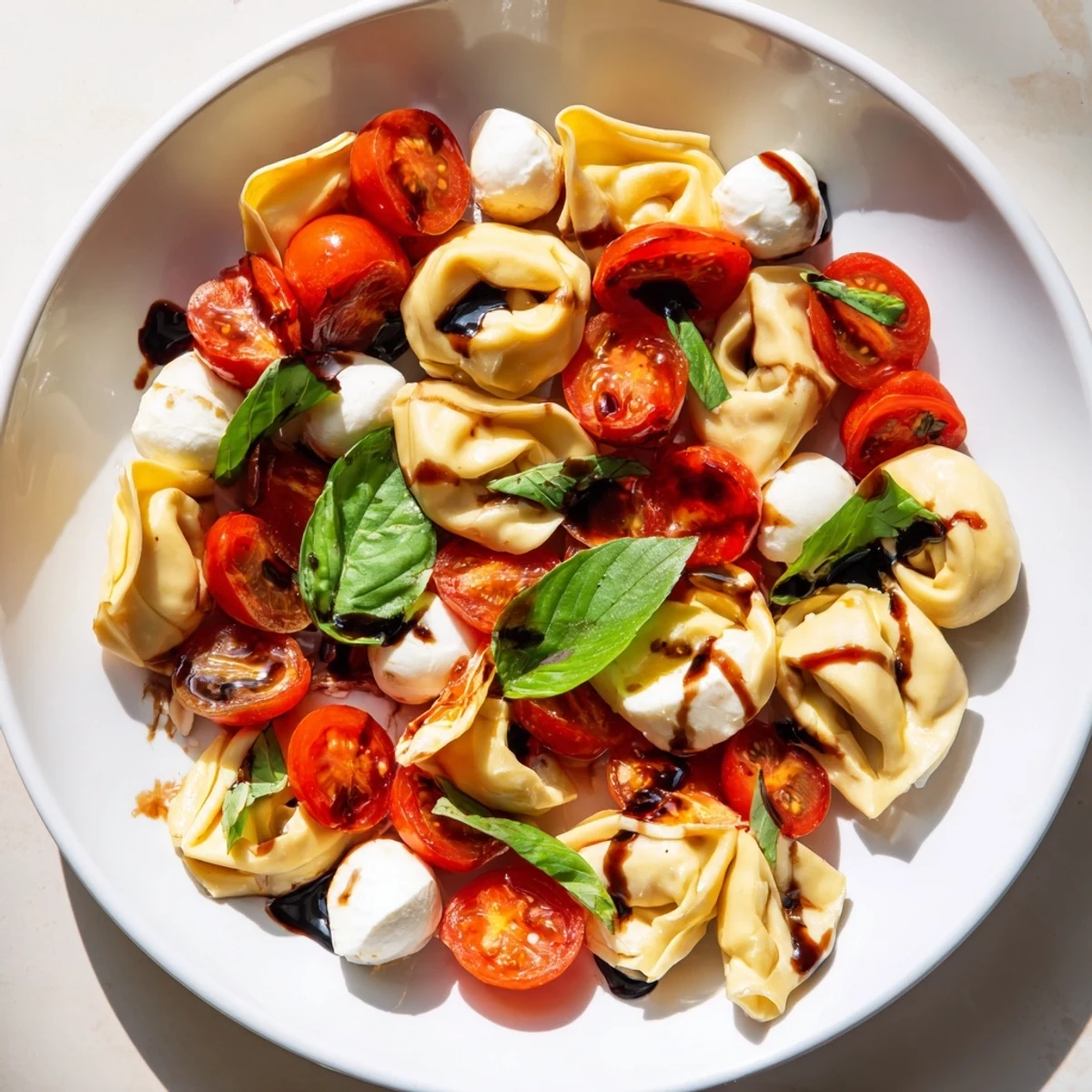 Vibrant summer bowl of al dente tortellini Caprese with fresh basil and balsamic glaze