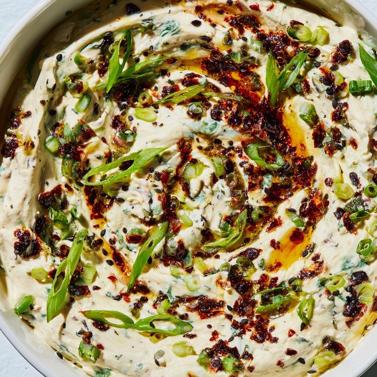 Rustic bowl of charred scallion and chili crisp dip garnished with fresh scallion greens