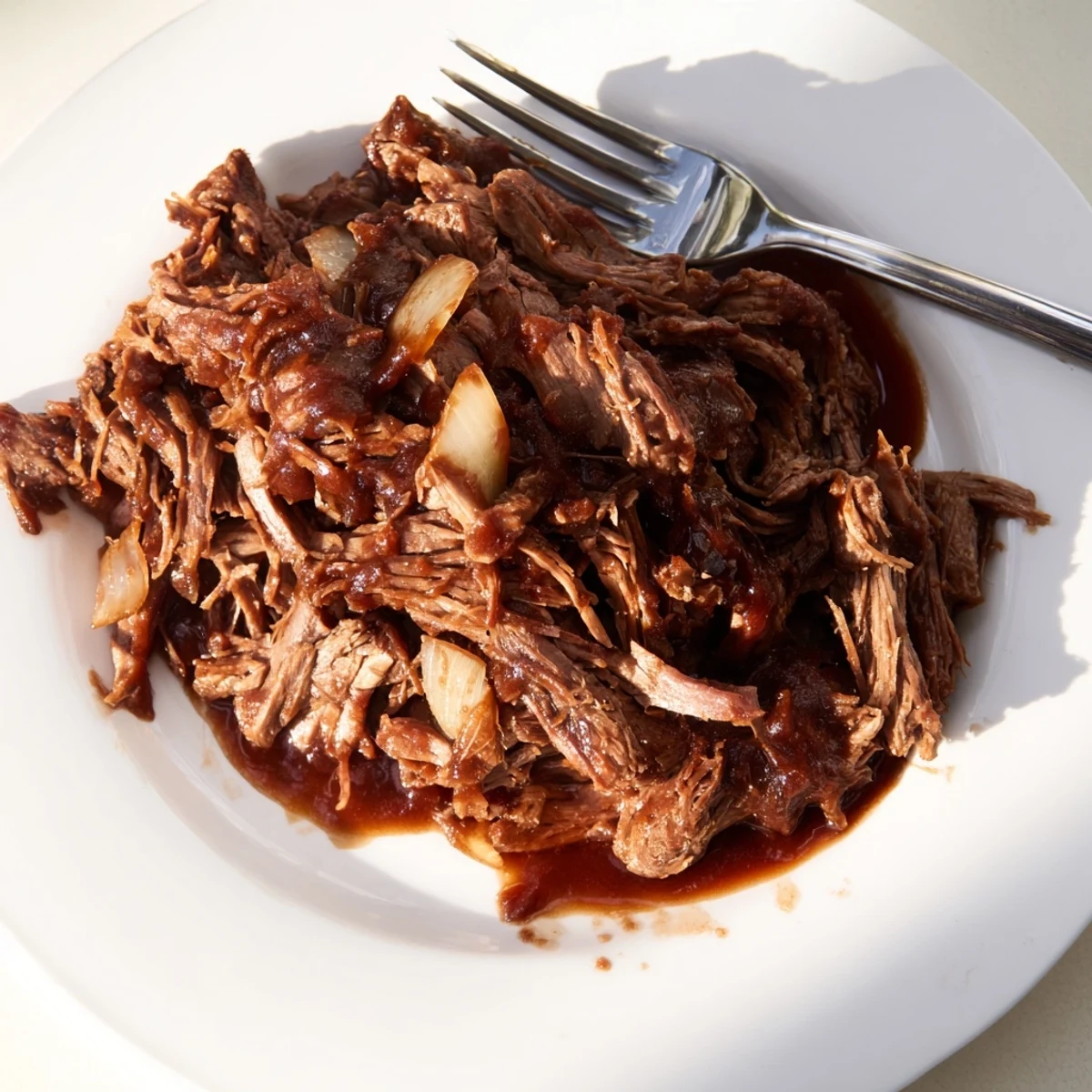 Tender Slow Cooker BBQ Pulled Beef smothered in rich, glossy barbecue sauce on a rustic plate
